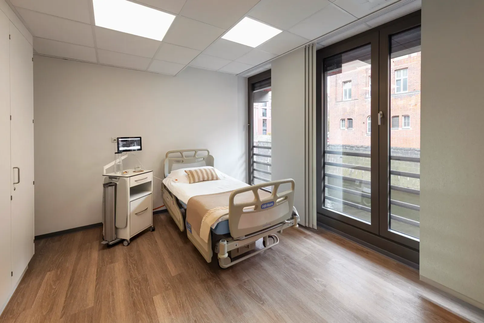 Patientenzimmer mit Pflegebett und Blick auf Backsteinhäuser