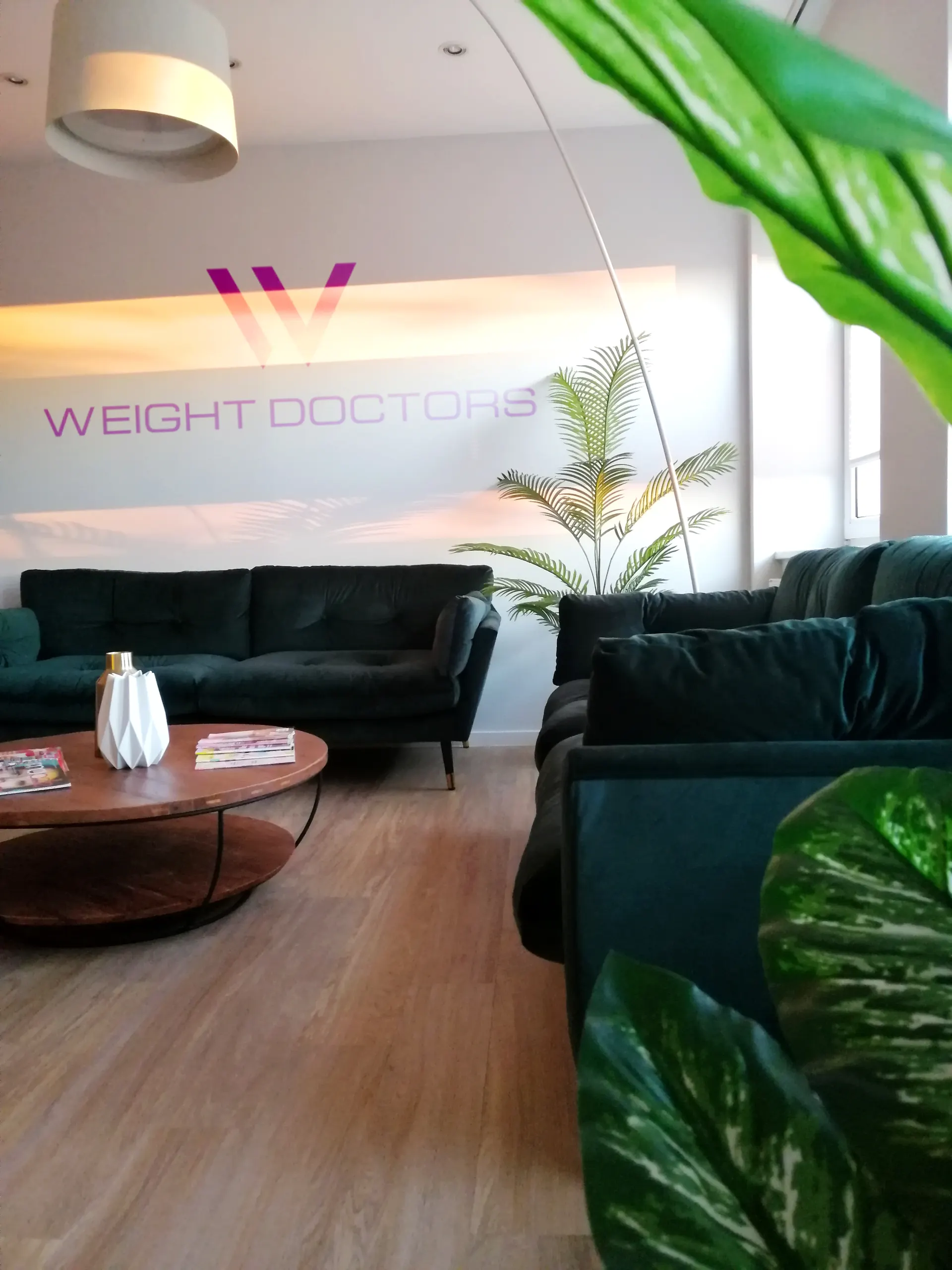 Lounge Weight Doctors® z zielonymi sofami i logo na ścianie